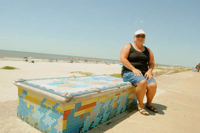 At Galveston’s busiest public beach, along the town seawall, 1st and 2nd grade children worked with Artist Boat to paint educational mosaics about local sea life on public benches. Kari Howard sits on one of these works of art and environmental education.